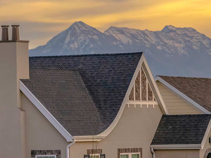 Large home during a sunset with a black shingle roof and a mountain in the background